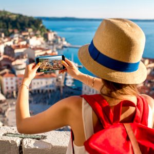 Young female traveler with red backpack and photo camera enjoying the view on Piran old town. Traveling in Slovenia